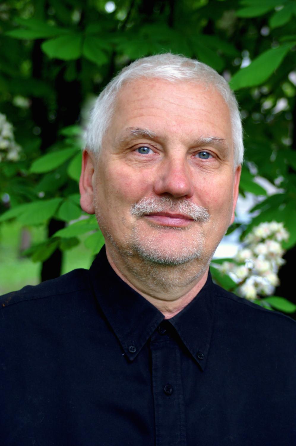Pianista Michał Korzistka w siwych włosach i czarnej koszuli pozuje na tle zieleni