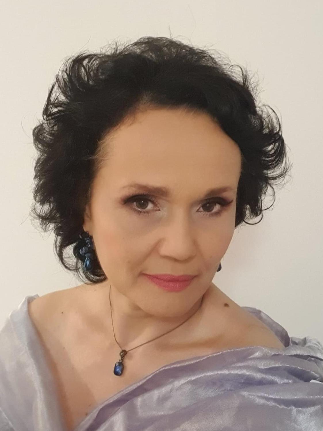 Śpiewaczka Dorota Lachowicz pozuje w jasno niebieskiej skukni, ma czarne, kręcone włosym, na szyji wisi naszyjnik